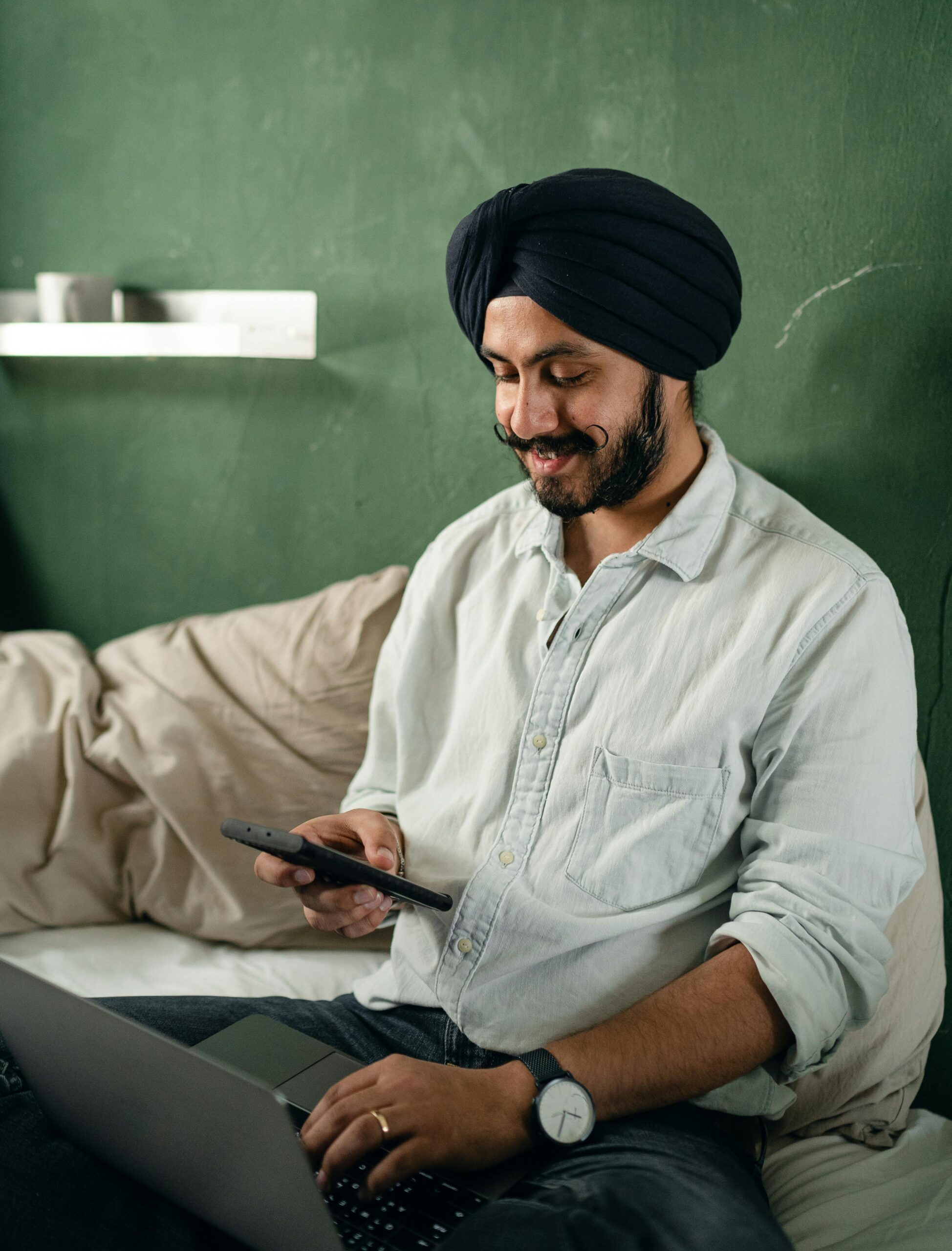 Positive man using laptop and smartphone on bed